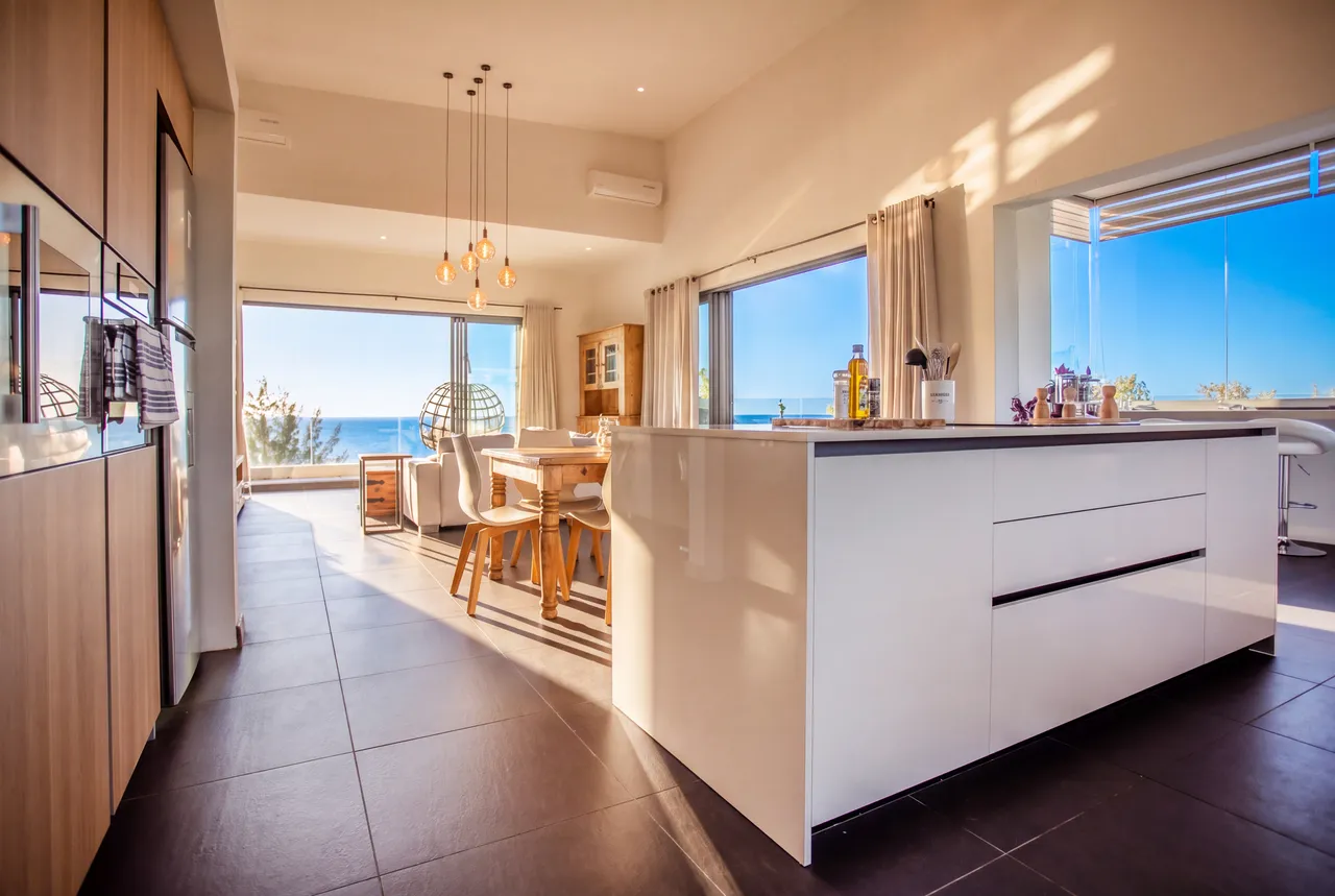 Cuisine ouverte avec un îlot central et vue sur la mer. Éclairage naturel abondant.