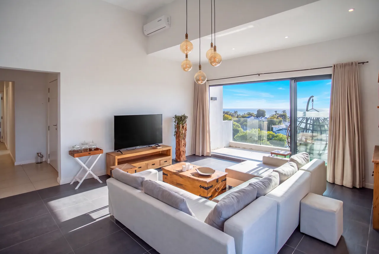 Espace salon avec grandes fenêtres et vue sur la mer. Éclairage naturel et mobilier confortable.