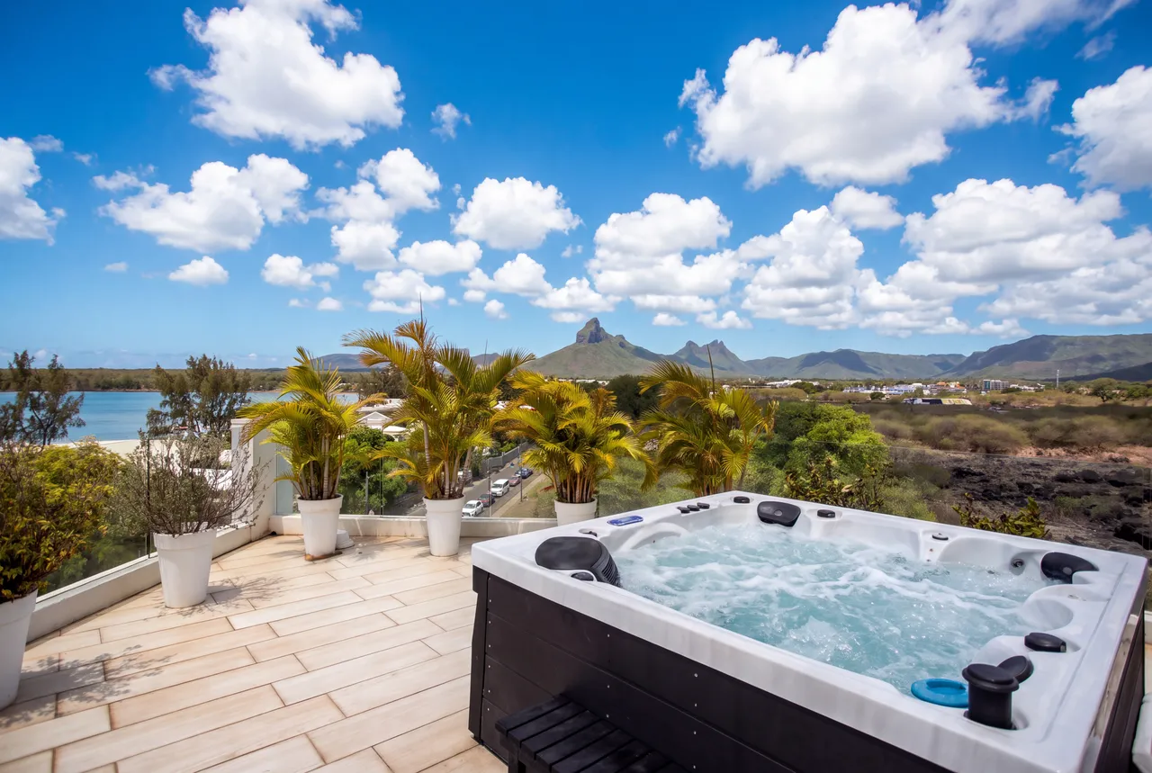 Jacuzzi sur la terrasse avec vue sur la montagne et la mer. Plantes en pots décorent l'espace.