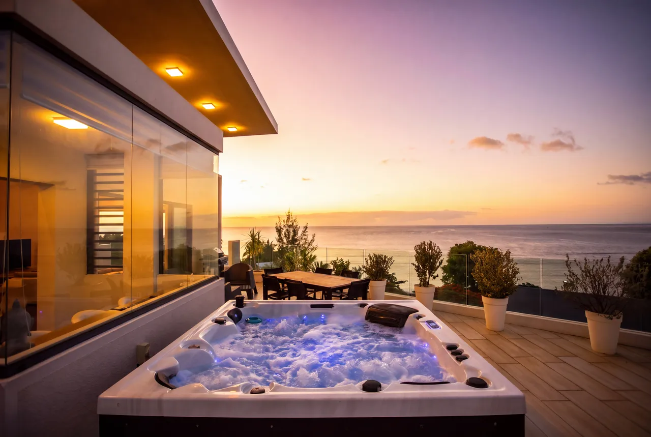 Jacuzzi avec vue sur la mer au coucher du soleil. Espace extérieur aménagé.