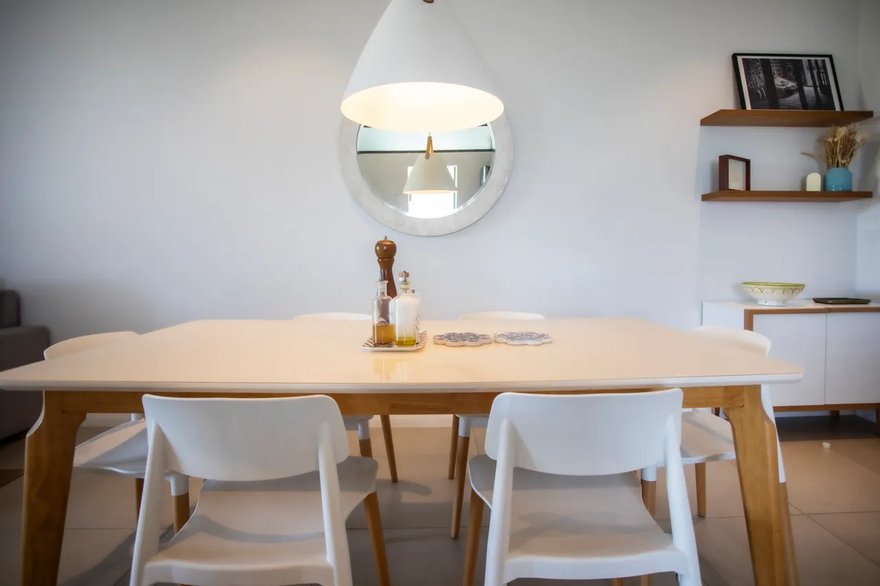 Table blanche en bois avec chaises en plastique empilables. Éclairage suspendu au-dessus.