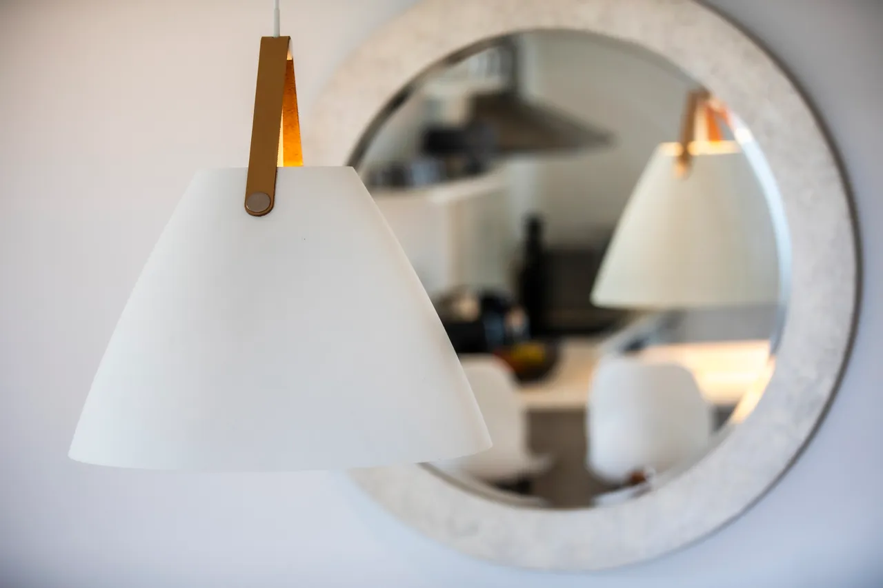 Luminaires blancs et miroir rond ajoutent une touche contemporaine au décor. Éclairage fonctionnel harmonisé avec le style minimaliste de l'espace.