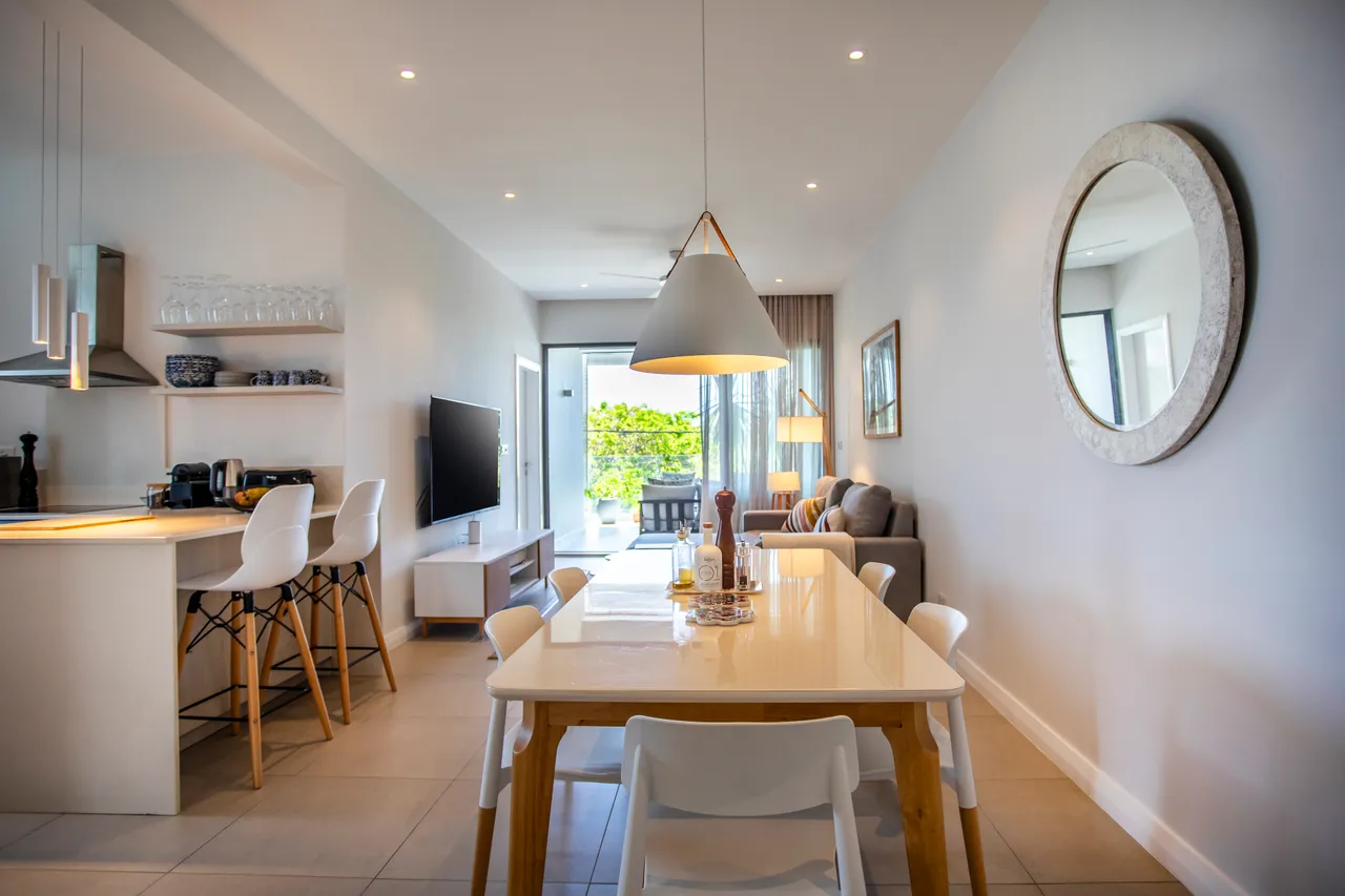 Espace repas avec table blanche et chaises modernes. Accès à une terrasse verdoyante.