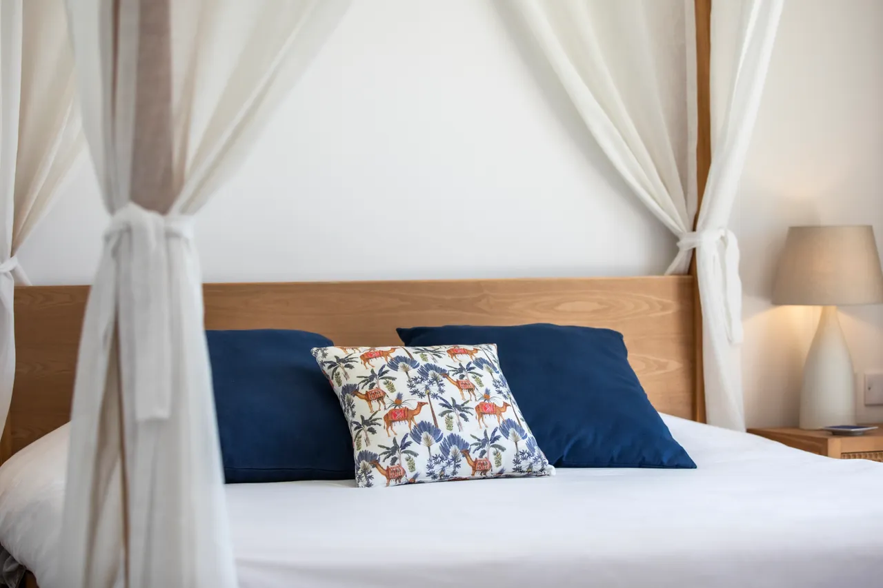 Literie blanche et coussins colorés ajoutent une touche de confort. Tête de lit en bois et lampe douce complètent l'agencement.