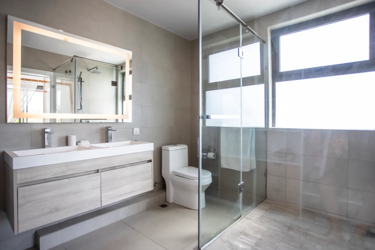 Salle de bain lumineuse avec fenêtres offrant une vue sur l'extérieur. Double vasque et rangement en bois clair.