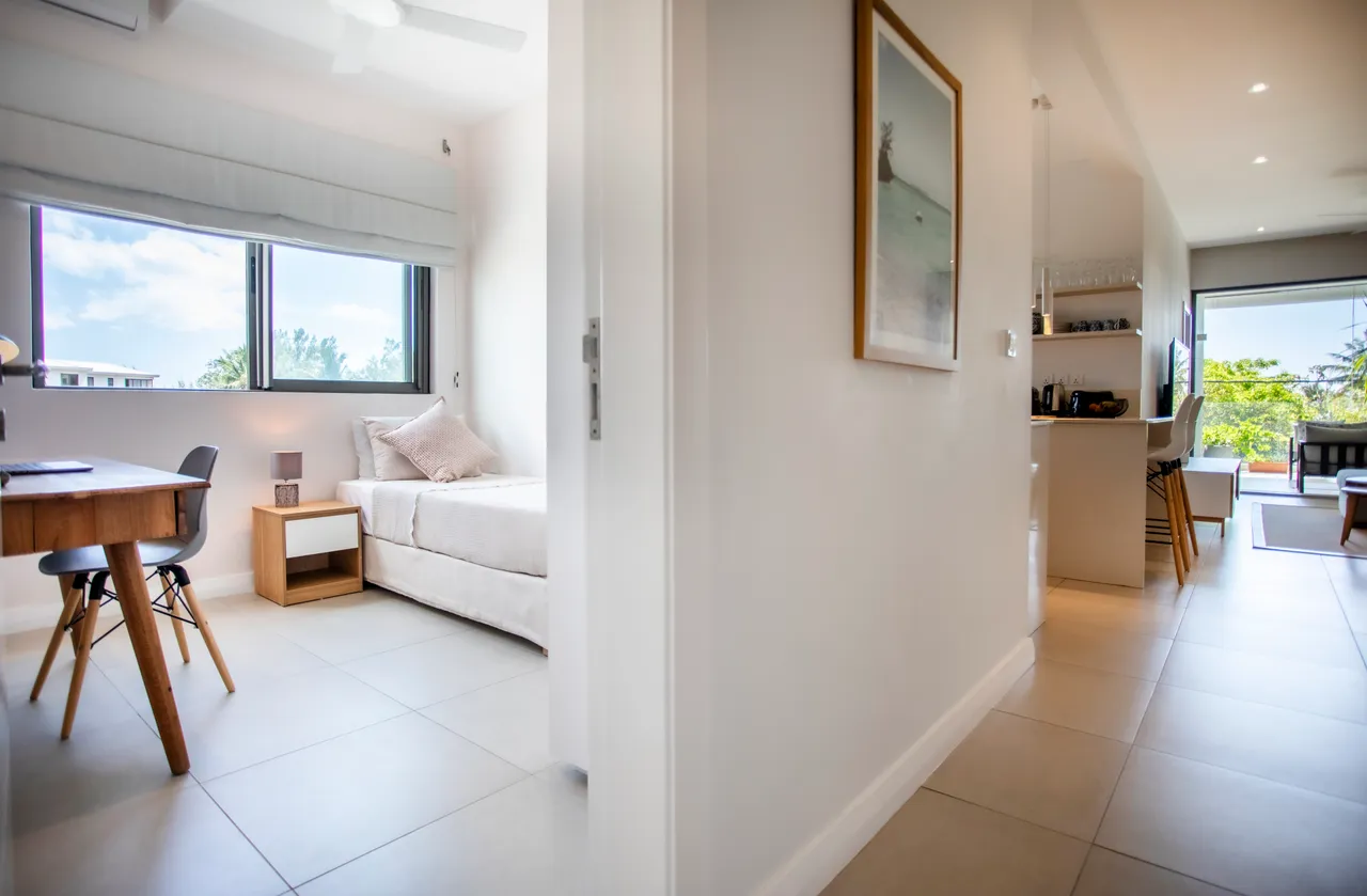 Couleurs claires et textures douces dominent cet espace. Coin bureau avec chaise contemporaine et lumière naturelle. Chambre dotée de lit simple et rangements intégrés. Vue sur l'extérieur depuis les fenêtres. Sol en carrelage facile d'entretien dans tout l'appartement.