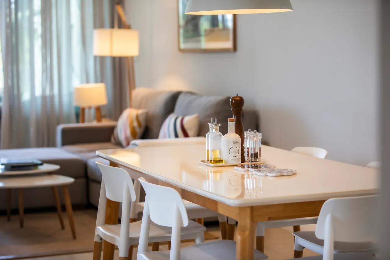 Espace repas avec table en bois et décor épuré. Éclairage suspendu au-dessus de la table.