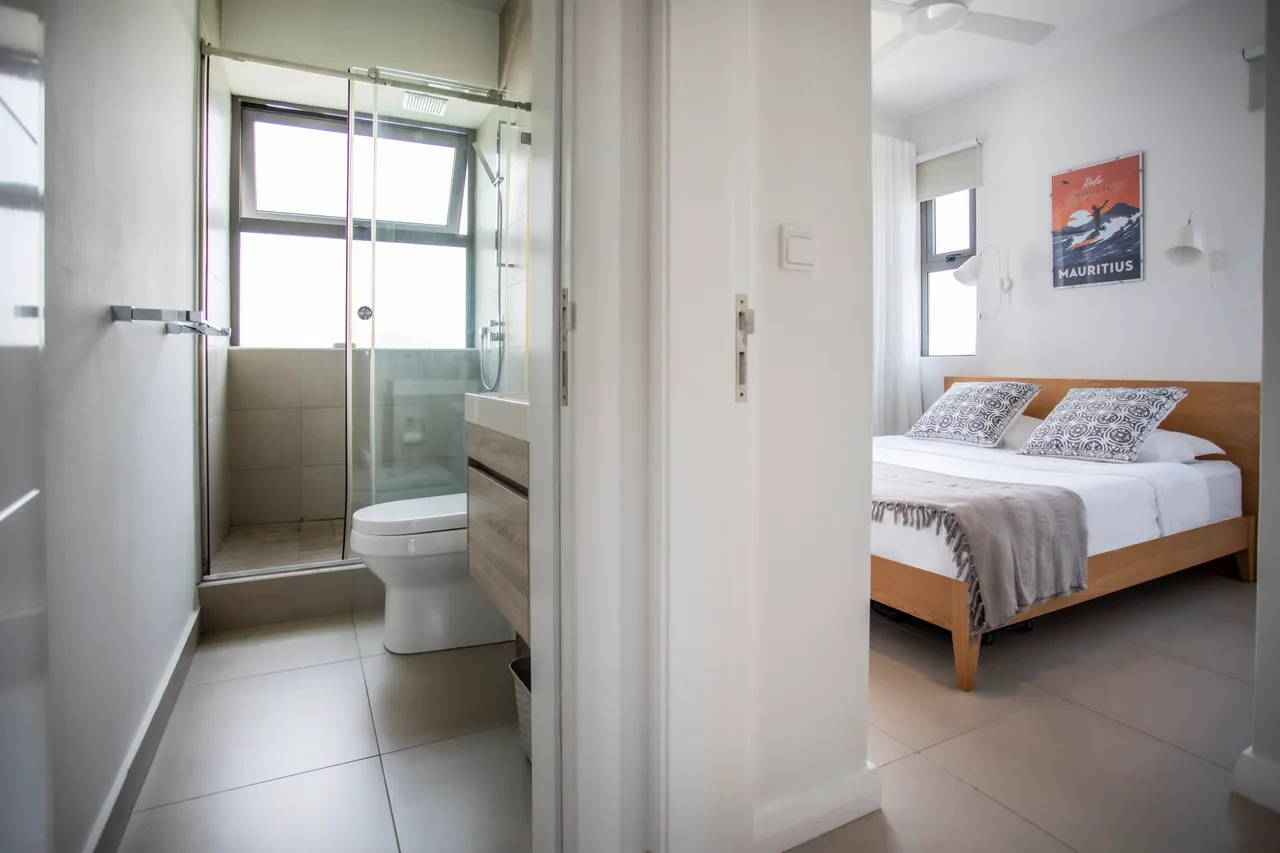 Chambre avec lit double, linge de lit clair et décoration minimaliste. Douche à l'italienne et lumière naturelle dans la salle de bain.