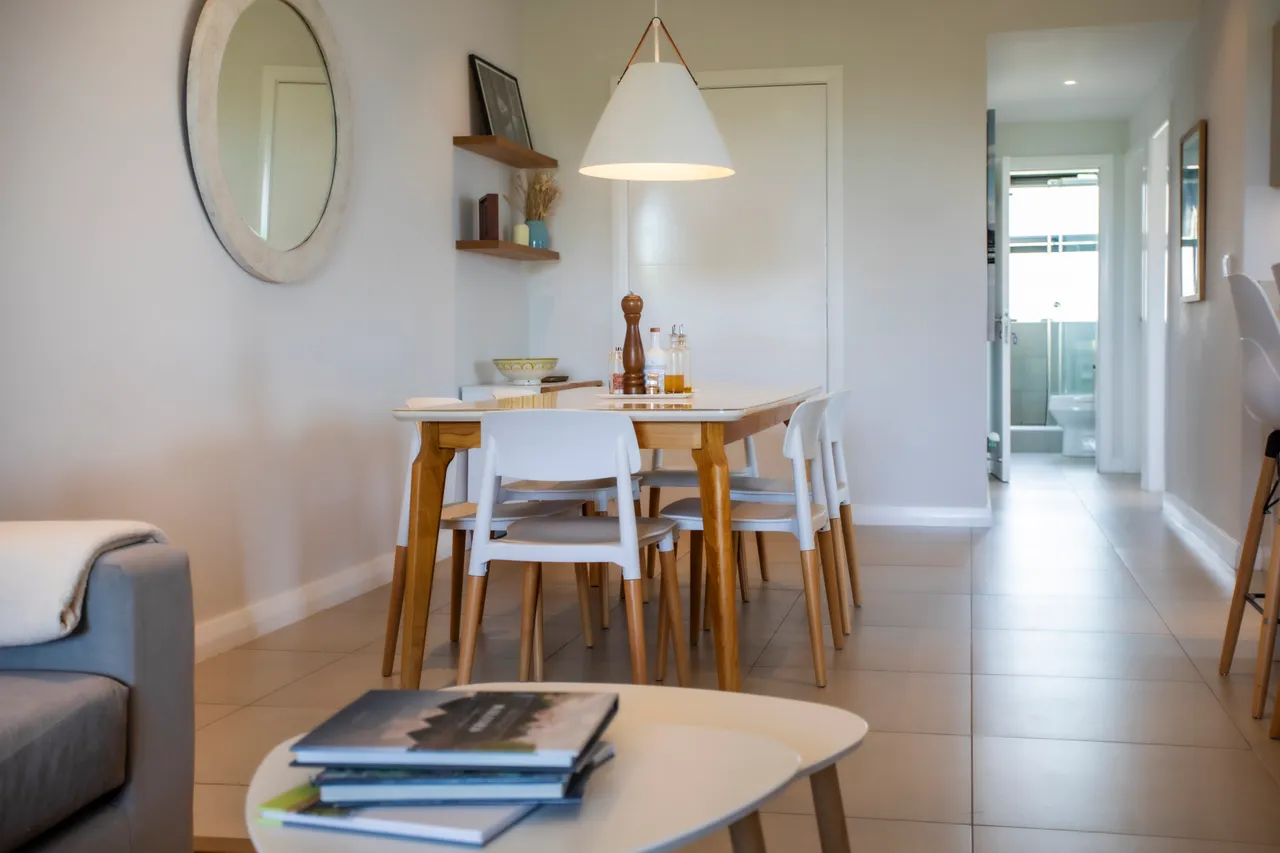 Sol carrelé et mobilier en bois clair dotent l'espace de repas d'un style sobre. Une lumière douce émane du plafonnier, créant une ambiance accueillante.