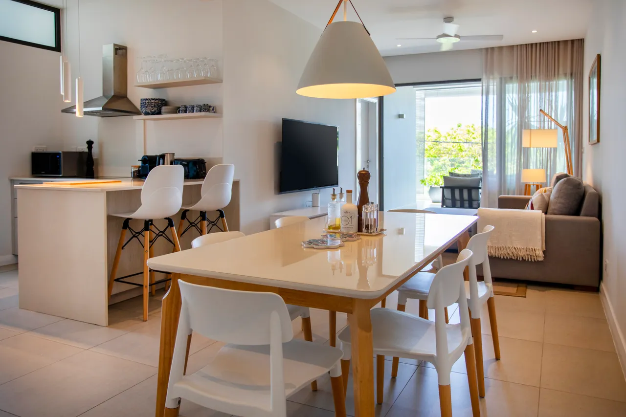 Espace repas avec table claire et chaises modernes. Cuisine ouverte avec bar et équipements.