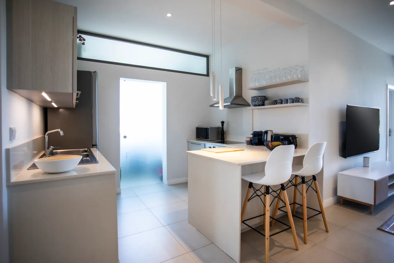 Plans clairs et surfaces lumineuses caractérisent cette cuisine fonctionnelle. Bar avec chaises hautes pour repas rapides. Équilibre entre modernité et praticité dans l'agencement.