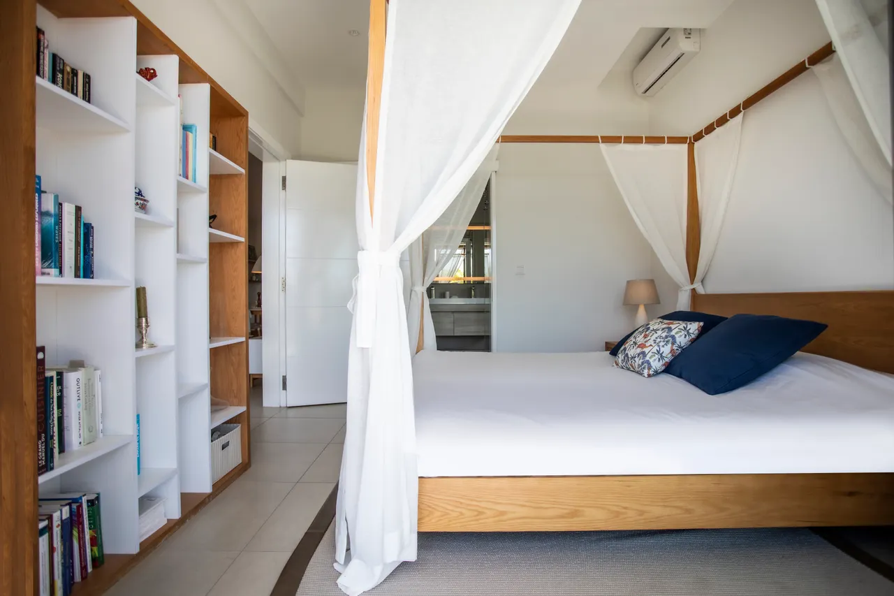 Tons neutres et mobilier en bois créent une ambiance sereine. Lit à baldaquin avec oreillers décoratifs et étagères intégrées.