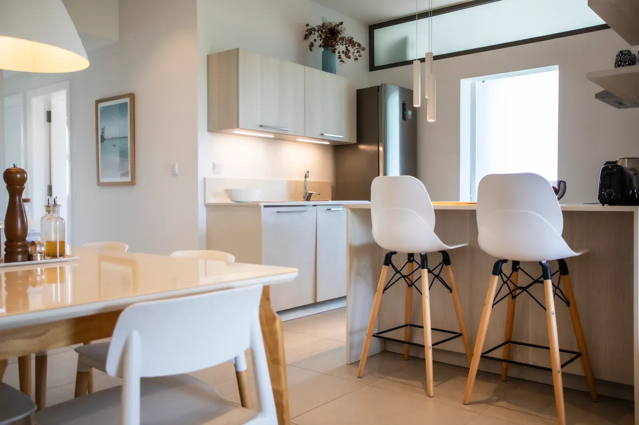 Cuisine équipée avec bar à petit-déjeuner et chaises hautes au design contemporain. Électroménagers intégrés et espace de rangement optimisé. Lumière naturelle grâce à une fenêtre.