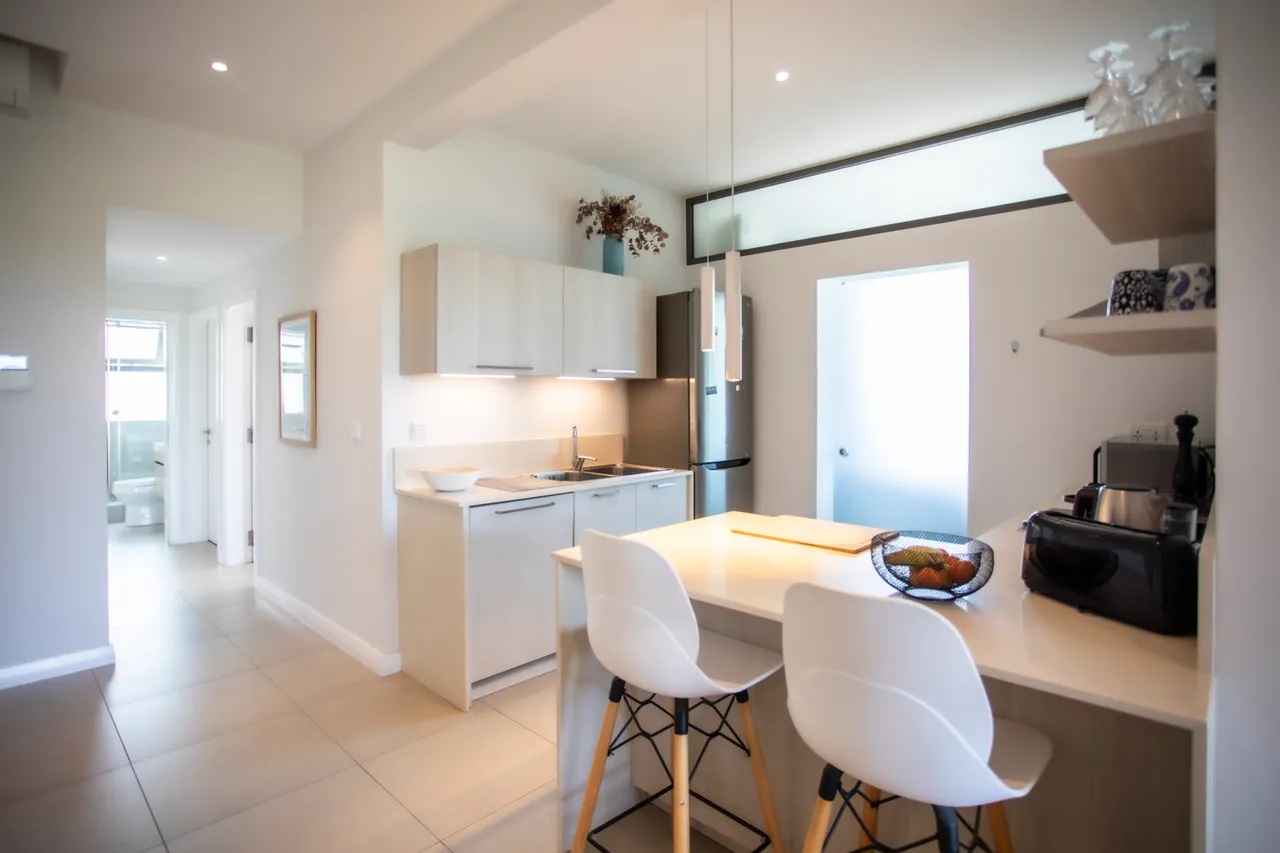 Cuisine ouverte avec plan de travail clair et bar à petit-déjeuner. Équipement moderne et lumière naturelle.