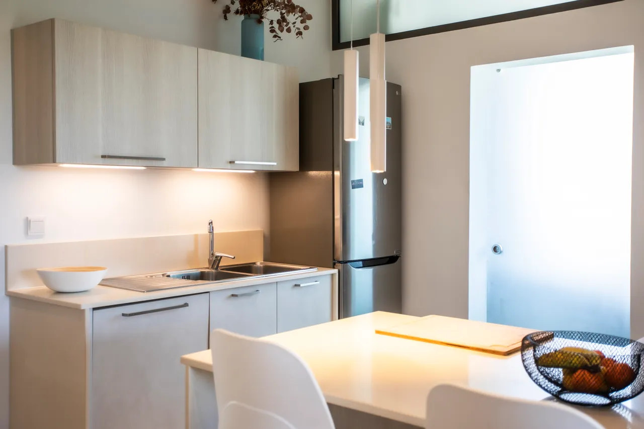 Cuisine minimaliste avec plans de travail clairs et rangements intégrés. Éclairage moderne au-dessus du comptoir.
