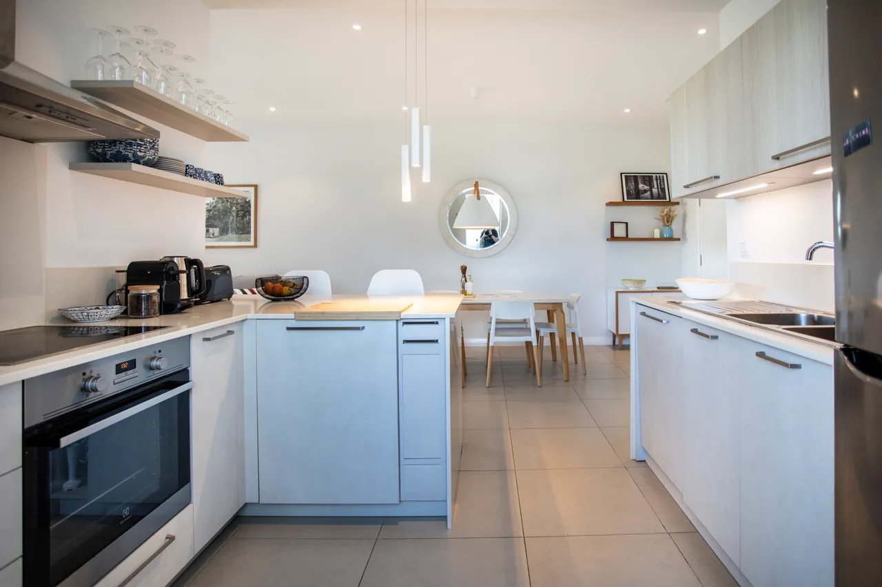 Cuisine bien équipée avec plans de travail clairs et rangements. Éclairage moderne accentue l'espace fonctionnel.