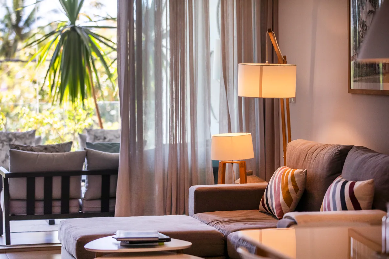 Tons chauds et textures douces créent une atmosphère accueillante. Canapé confortable avec coussins colorés et éclairage doux.