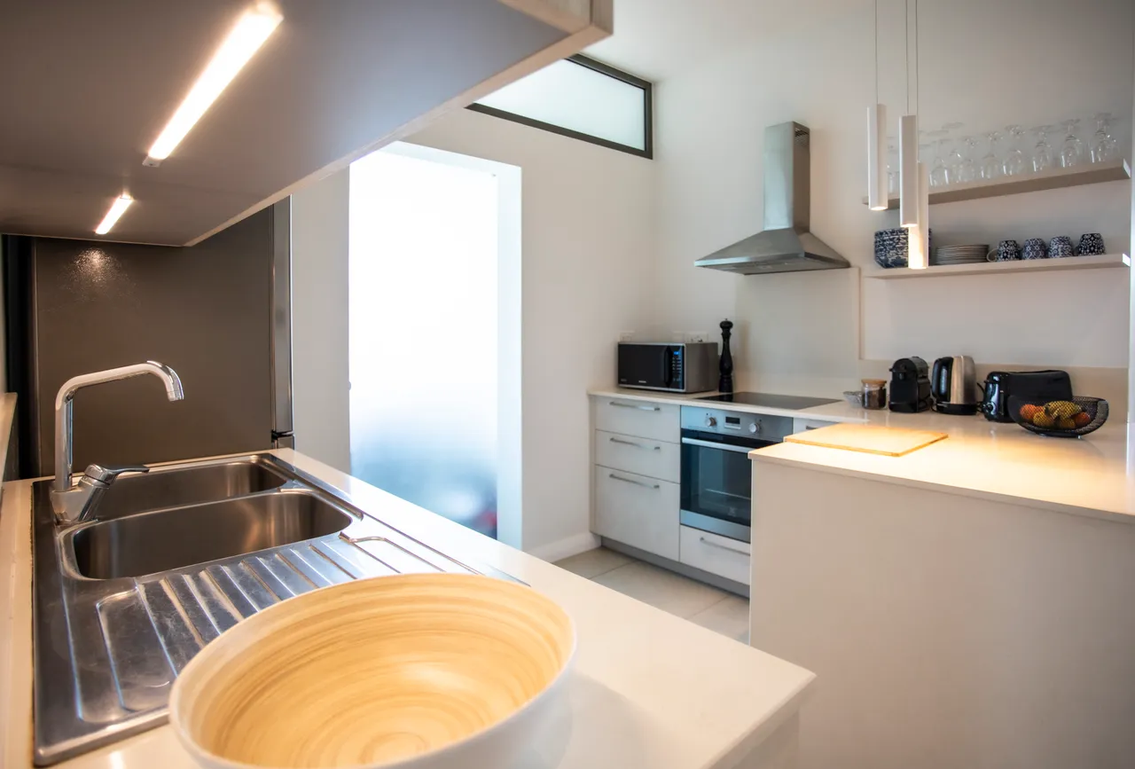 Cuisine moderne avec évier en inox et plans de travail clairs. Équipements fonctionnels et agencement pratique.