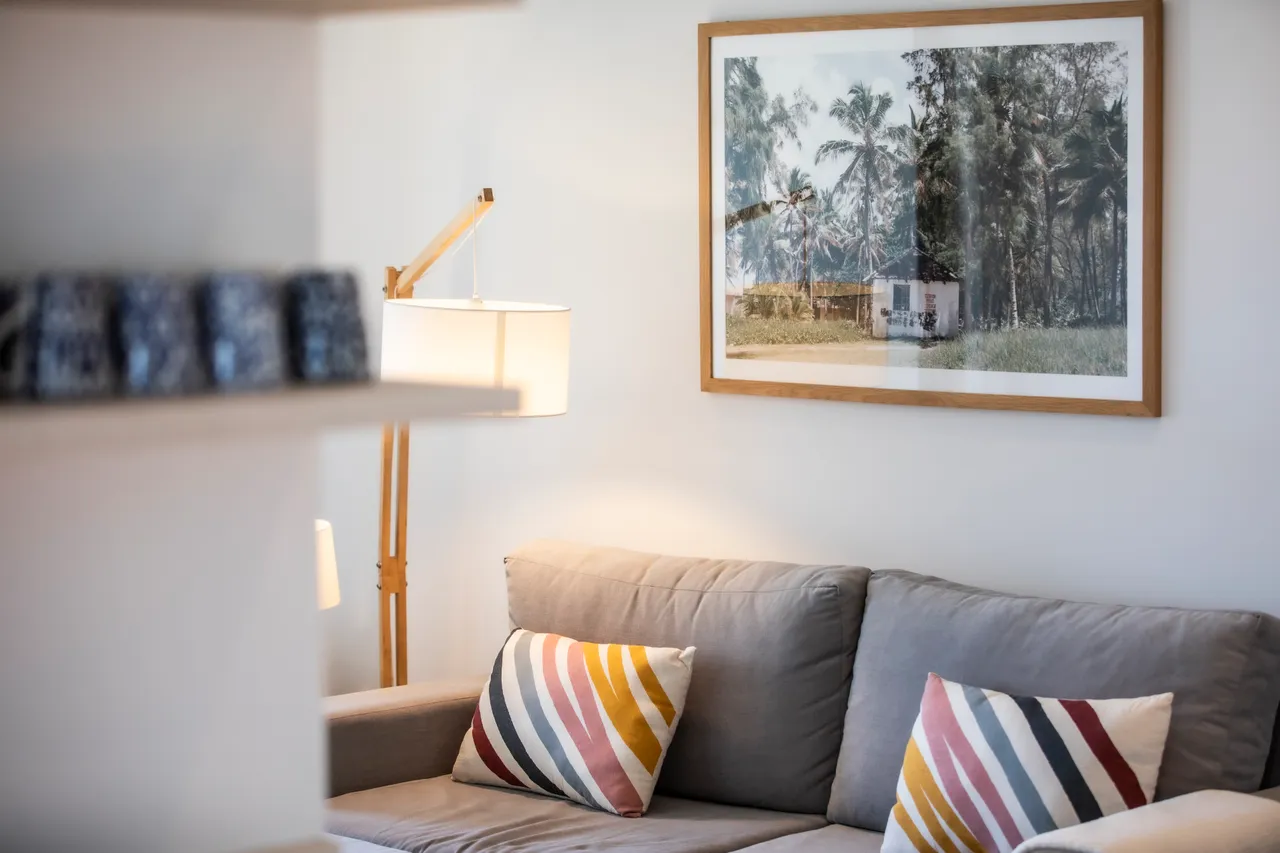 Canapé gris avec coussins rayés, éclairage doux provenant d'une lampe sur pied. Décoration murale en bois et photographies.