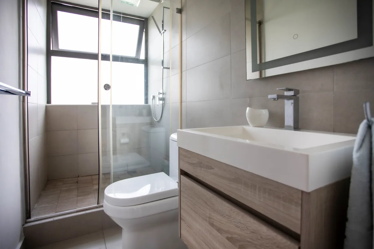 Couleurs neutres et matériaux modernes dans cette salle de bain. Douche à l'italienne avec paroi en verre et robinetterie contemporaine. Meuble sous-vasque en bois clair offrant du rangement.
