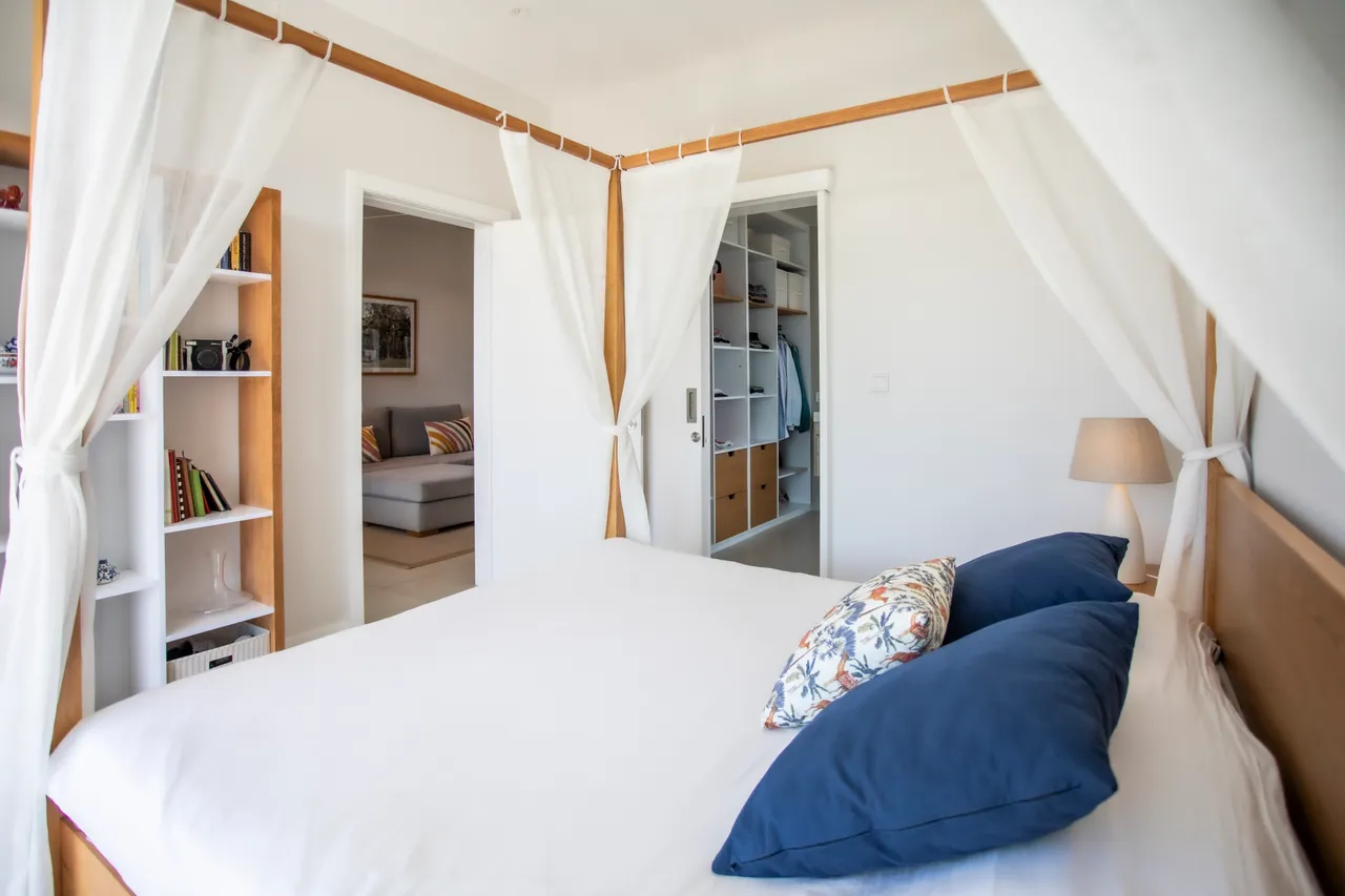 Chambre avec lit à baldaquin et draps en lin. Étagères ouvertes pour le rangement.