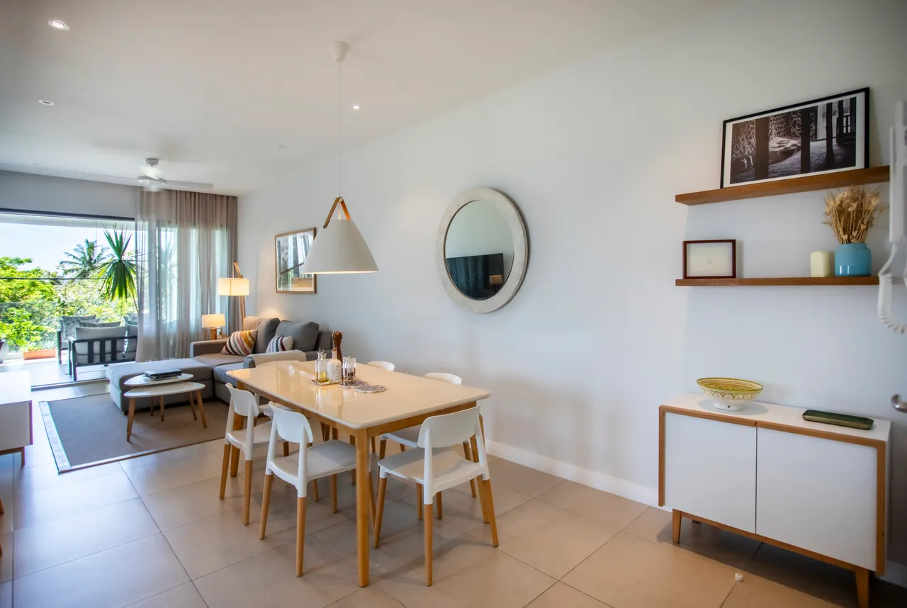 Tons clairs et mobilier moderne dans une salle à manger fonctionnelle. Grande table entourée de chaises blanches, miroir rond et étagères en bois ajoutent du style.