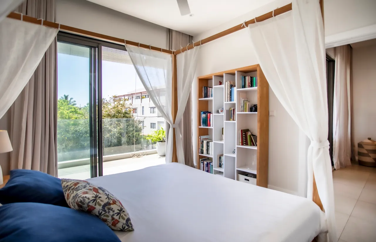 Chambre lumineuse avec accès direct à un balcon. Étagères intégrées pour le rangement des livres.