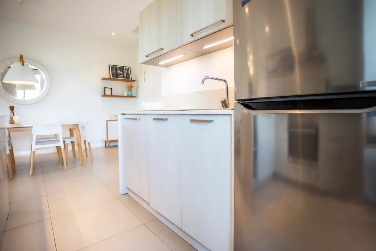 Cuisine avec meubles en bois clair et plan de travail lumineux. Électroménagers modernes et rangement optimisé.
