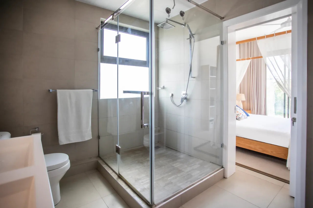 Douche à l'italienne avec paroi en verre et carrelage clair. Serviettes blanches bien disposées.