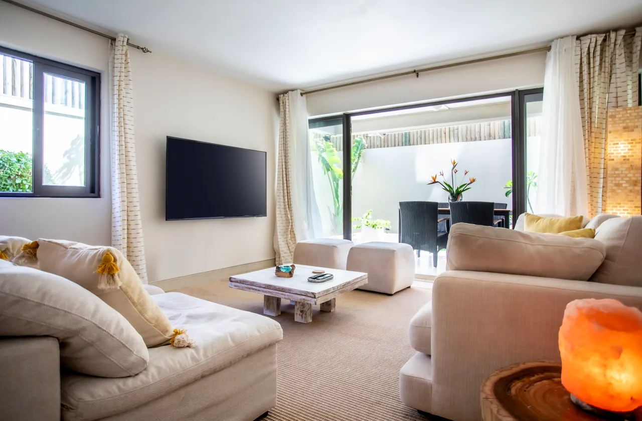 Lumière naturelle inonde l'espace grâce aux grandes ouvertures sur l'extérieur.  

Canapés clairs et confortables créent un coin accueillant pour se détendre.  

Table basse en bois apportant une touche naturelle à l'intérieur.  

Plantes d'intérieur ajoutent une note de verdure et de fraîcheur.  

Accès direct à la terrasse, favorisant les moments