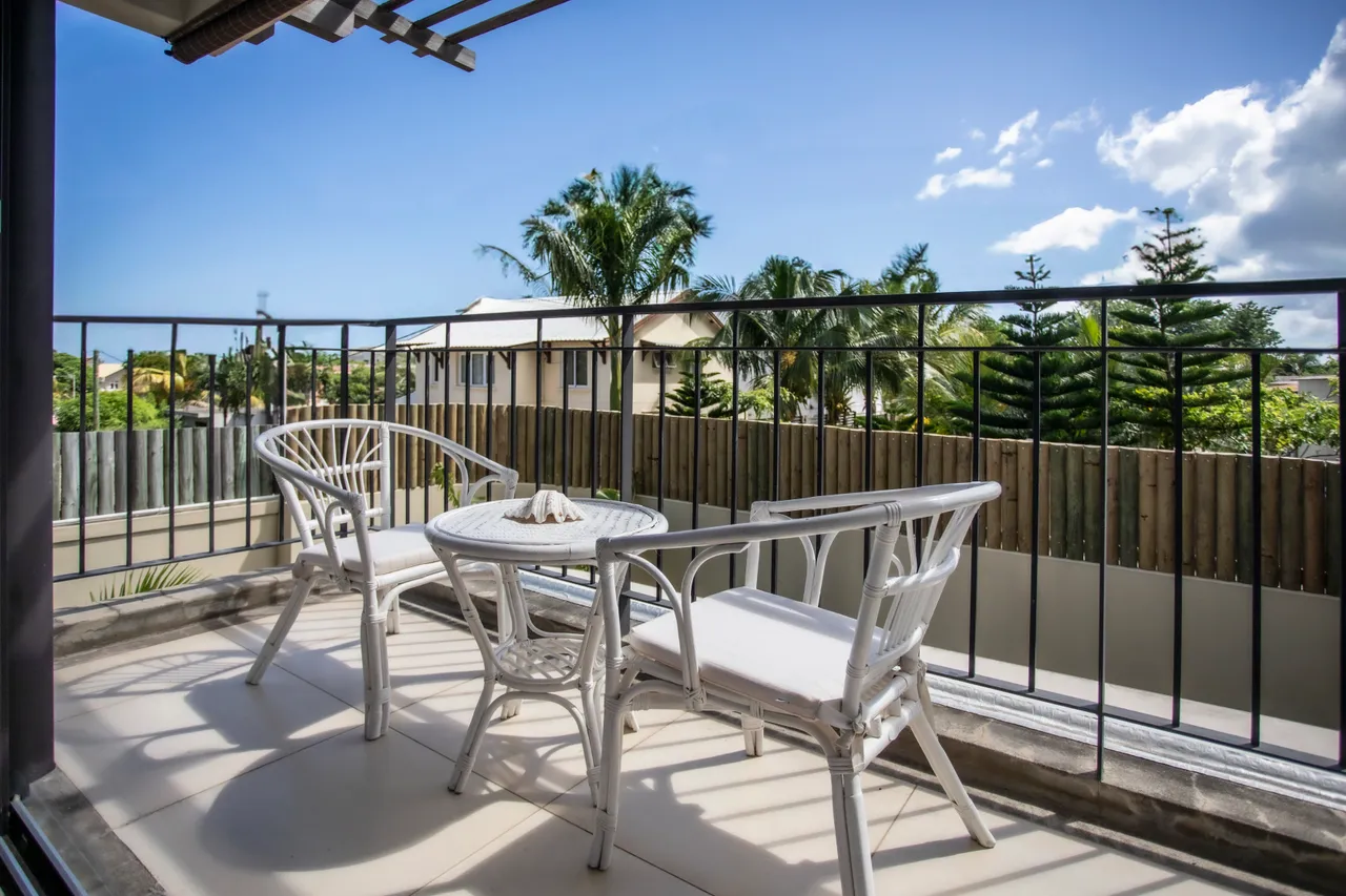 Terrasse avec chaises en rotin et table pour profiter de l'extérieur.  

Vue dégagée sur la végétation environnante grâce à la balustrade.  

Accès direct depuis l'intérieur, facilitant les repas en plein air.  

Sol carrelé offrant une surface confortable pour s'installer.  

Ombre partielle fournie par le dispositif de protection au-dessus.