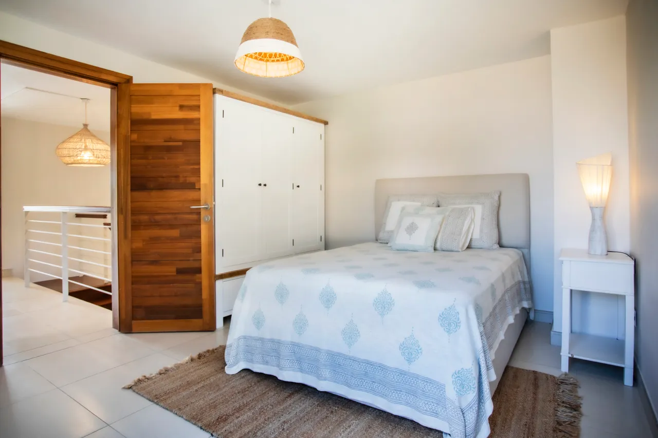 Chambre avec lit double et rangement intégré, offrant un espace fonctionnel.  

Éclairage doux provenant d'une lampe sur la table de chevet.  

Tapis tissé au sol ajoutant une texture chaleureuse à la pièce.  

Porte en bois apportant une touche naturelle à l'entrée.  

Fenêtre large laissant entrer la lumière naturelle, créant une ambiance lumineuse.
