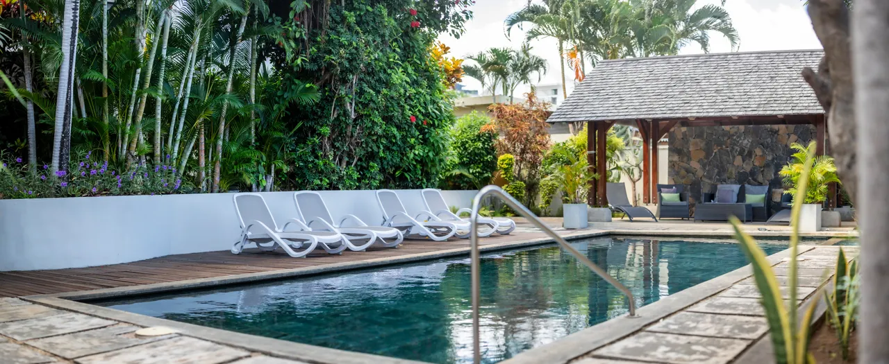 Espace extérieur avec piscine entourée de chaises longues pour se reposer.  
Terrasse en bois facilement accessible depuis l'entrée de la piscine.  
Végétation dense apportant une touche de nature à l'environnement.  
Coin salon abrité offrant un espace ombragé pour se détendre.  
Ambiance paisible favorisée par le bruit de l'eau et la verdure environnante