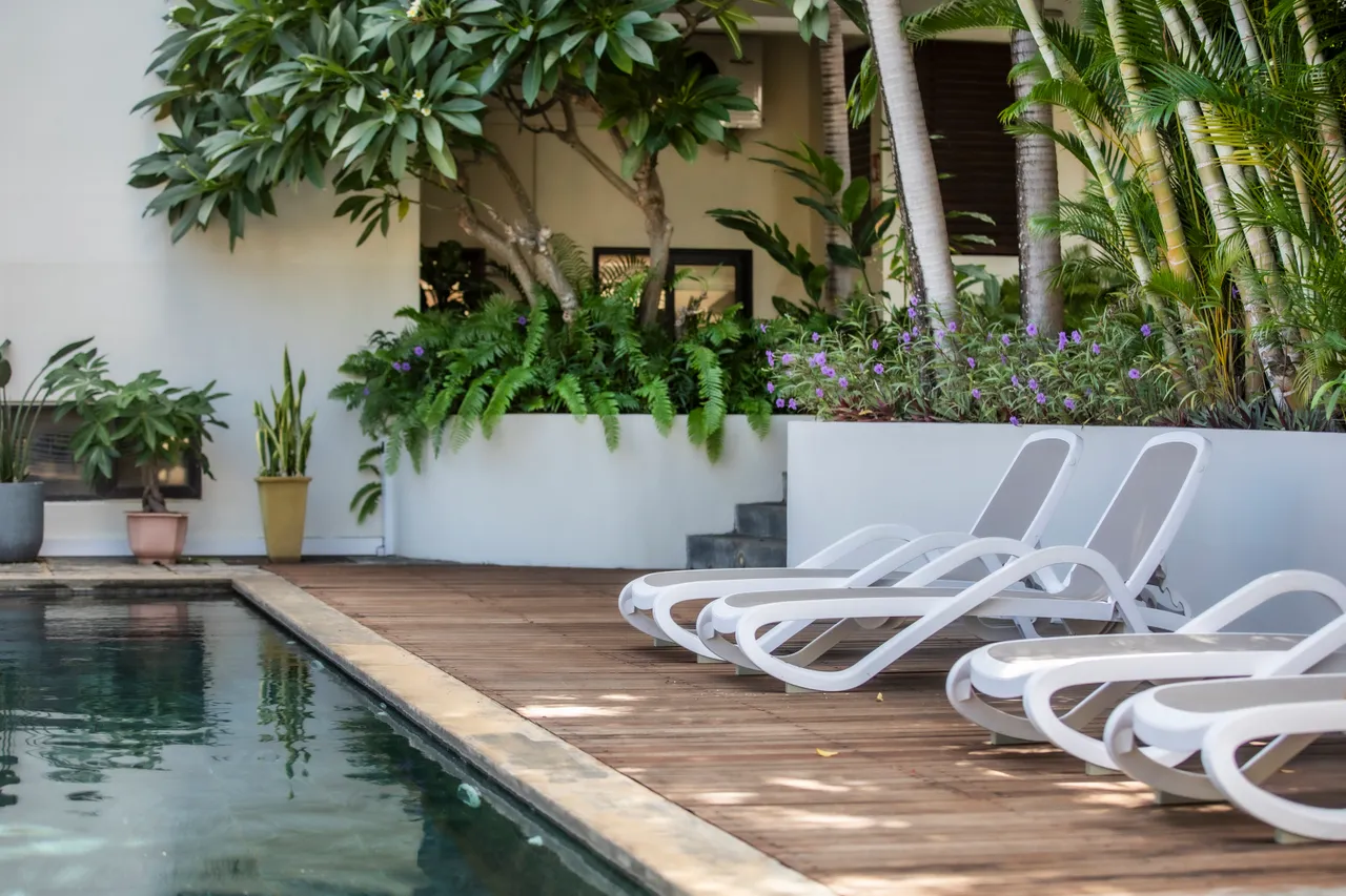 Espace extérieur avec chaises longues blanches, idéal pour se reposer au bord de la piscine.  
Végétation tropicale créant une atmosphère relaxante autour de l'eau.  
Terrasse en bois fournissant un accès direct à la piscine.  
Plantes en pot ajoutant une touche de verdure à l'environnement.  
Ambiance tranquille favorisée par le cadre naturel et
