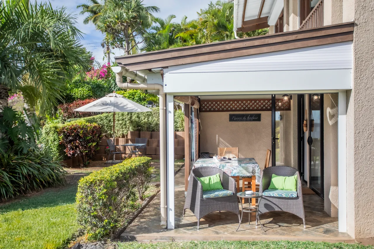 Espace extérieur avec fauteuils en rotin et parasol. Vue sur le jardin.