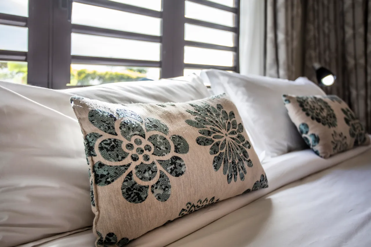 Coussins décoratifs avec motifs floraux sur le lit double. 

Linge de lit blanc et oreillers en tissu doux.