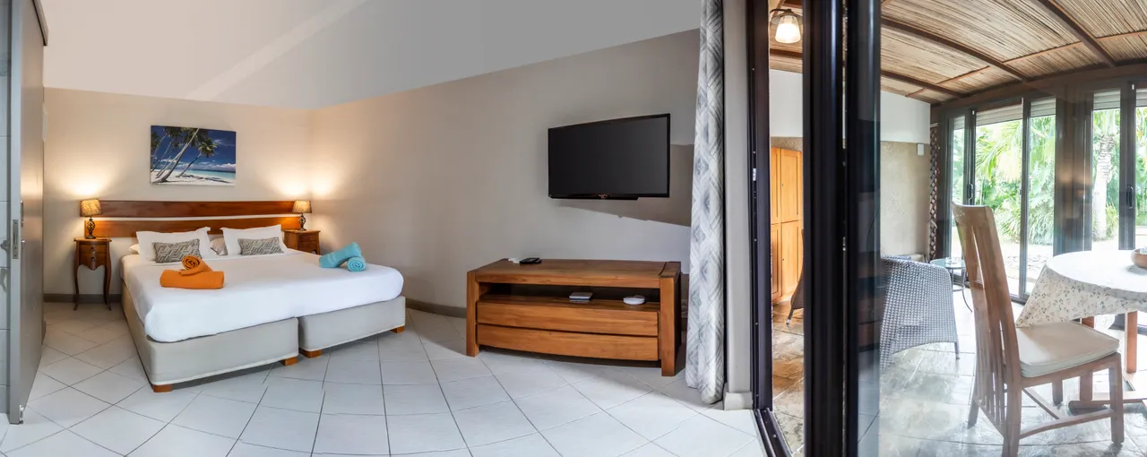 Chambre avec grand lit, mobilier en bois et lumière naturelle. Télévision à écran plat et accès direct à l'extérieur.