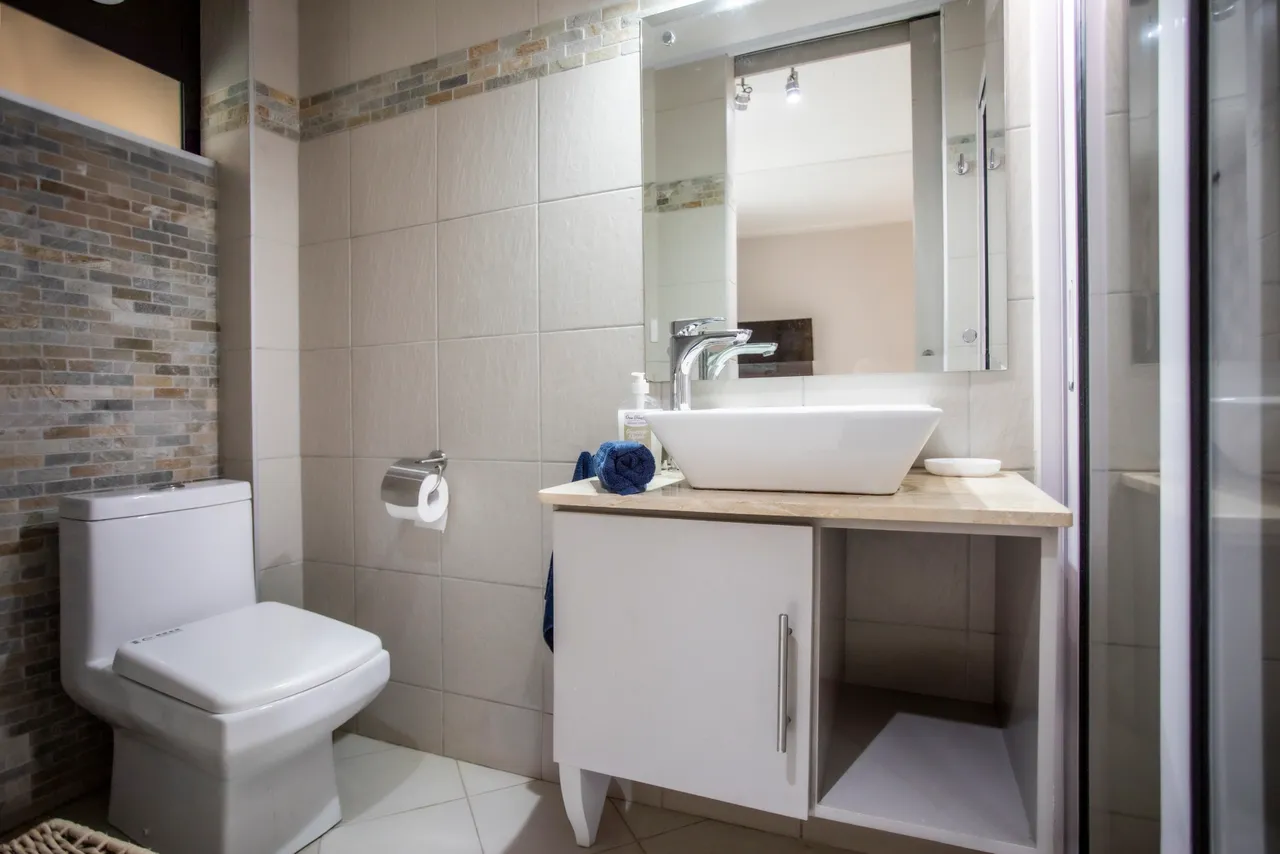 Salle de bain avec carrelage clair et vasque sur un meuble moderne. Douche séparée et lumière naturelle.
