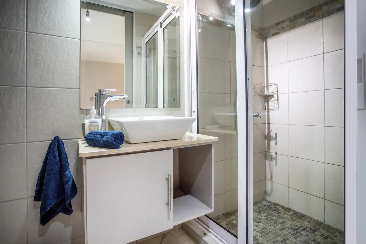 Salle de bain avec carrelage clair, vasque moderne et douche vitrée. Espace de rangement intégré.
