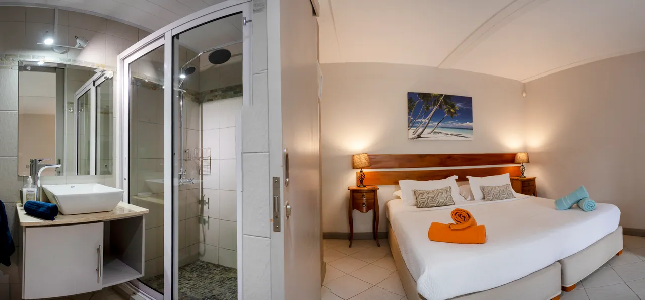 Chambre avec lit double, éclairage doux et décor minimaliste. Salle de bain attenante avec douche vitrée.
