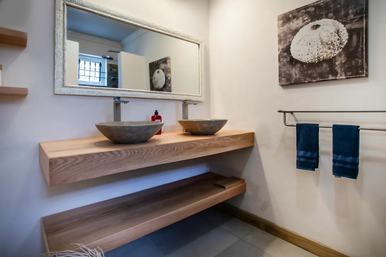 Salle de bain : Deux vasques sur un meuble en bois clair et miroir décoratif.