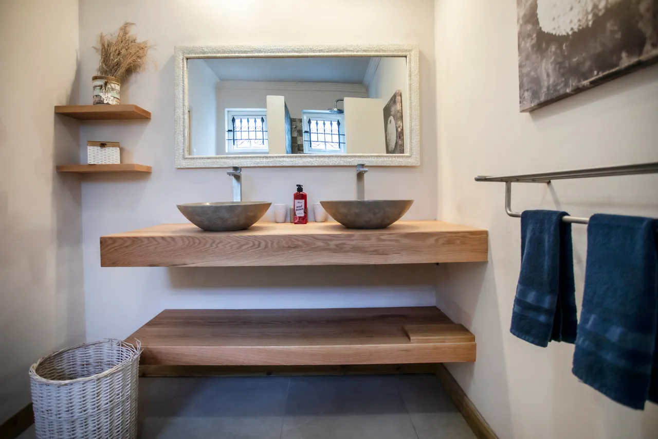 Salle de bain avec deux vasques en pierre sur un meuble en bois clair.