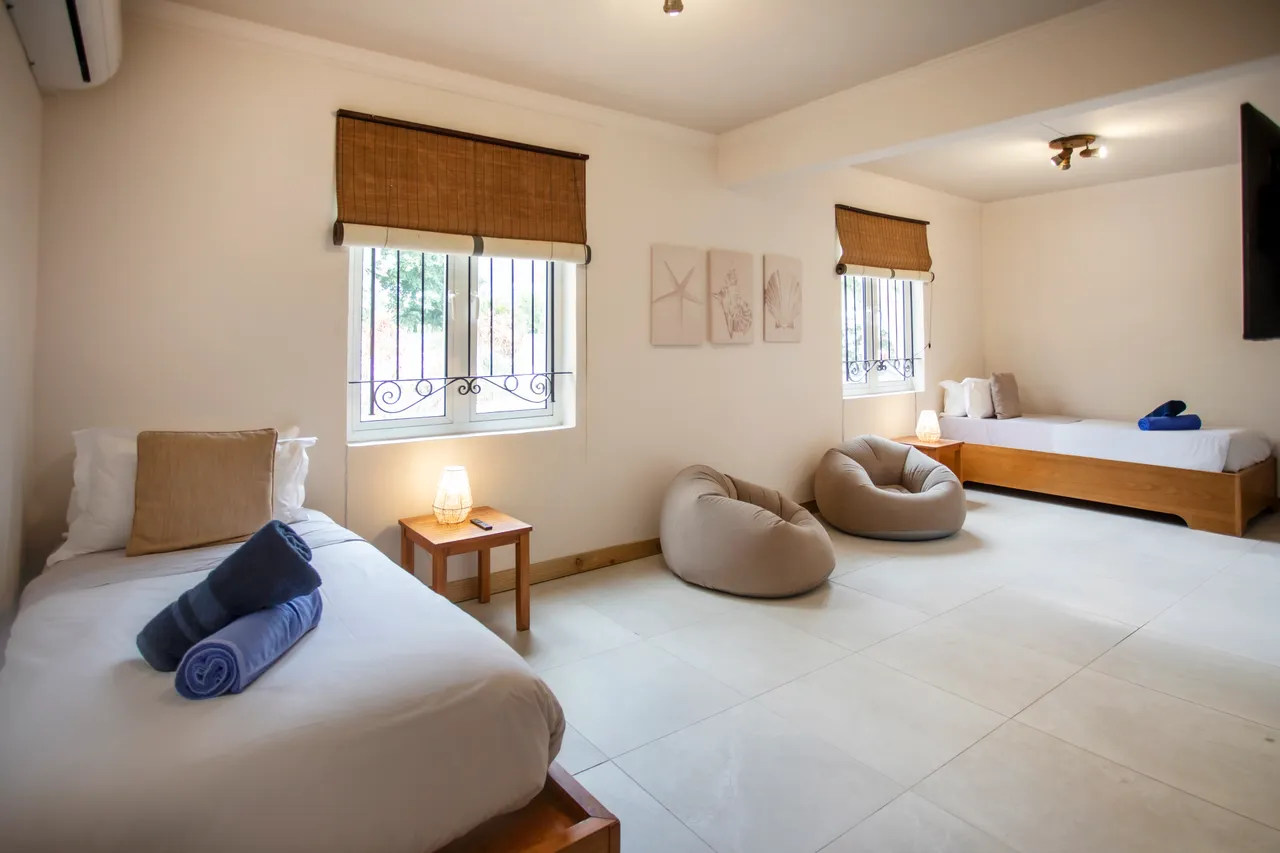 Chambre spacieuse avec deux lits et coin détente avec poufs.