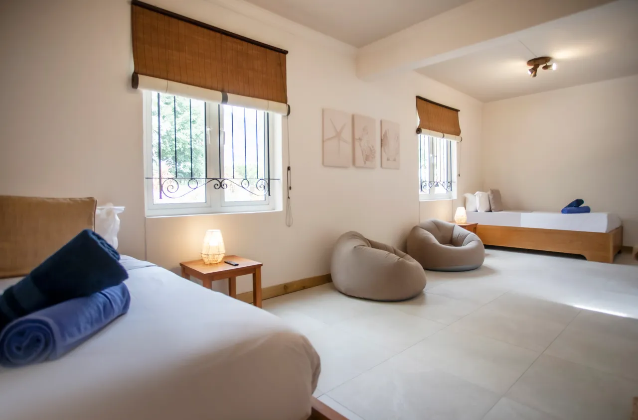 Chambre lumineuse avec des lits simples et des poufs au sol.