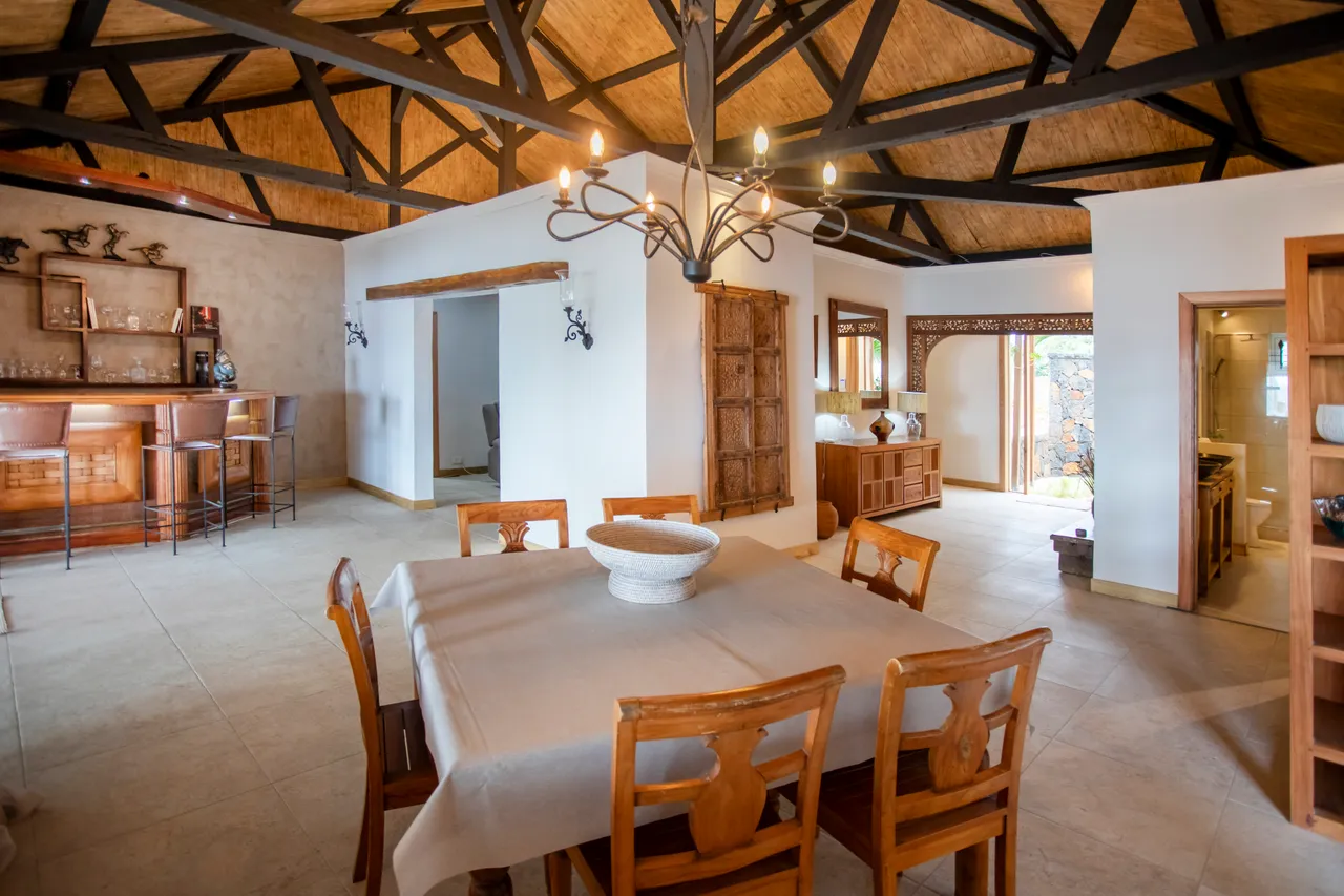 Espace repas avec table en bois et chaises sculptées. Plafond en bois voûté visible.