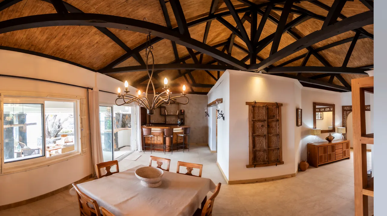 Lumière naturelle abondante grâce aux grandes fenêtres. Espace repas avec table en bois et bar attenant. Plafond en bois avec poutres apparentes.