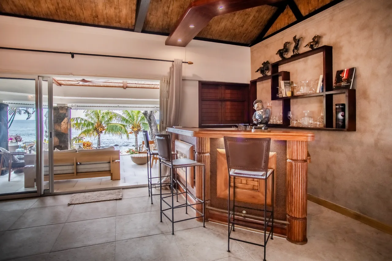 Espace repas avec bar en bois et tabourets, vue sur la plage. Ouverture sur la terrasse et le jardin.