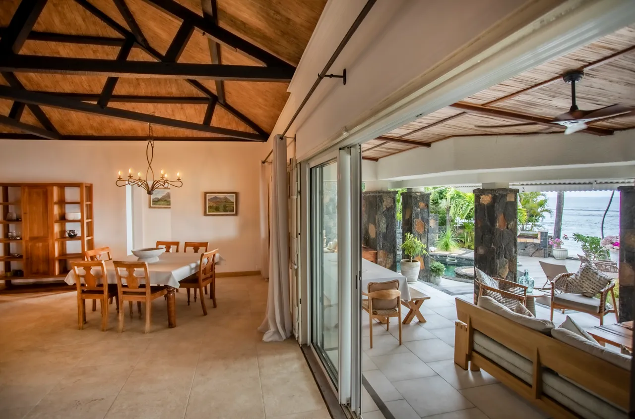 Espace repas lumineux avec grandes fenêtres ouvrant sur l'extérieur. Mobilier en bois sobre et fonctionnel.