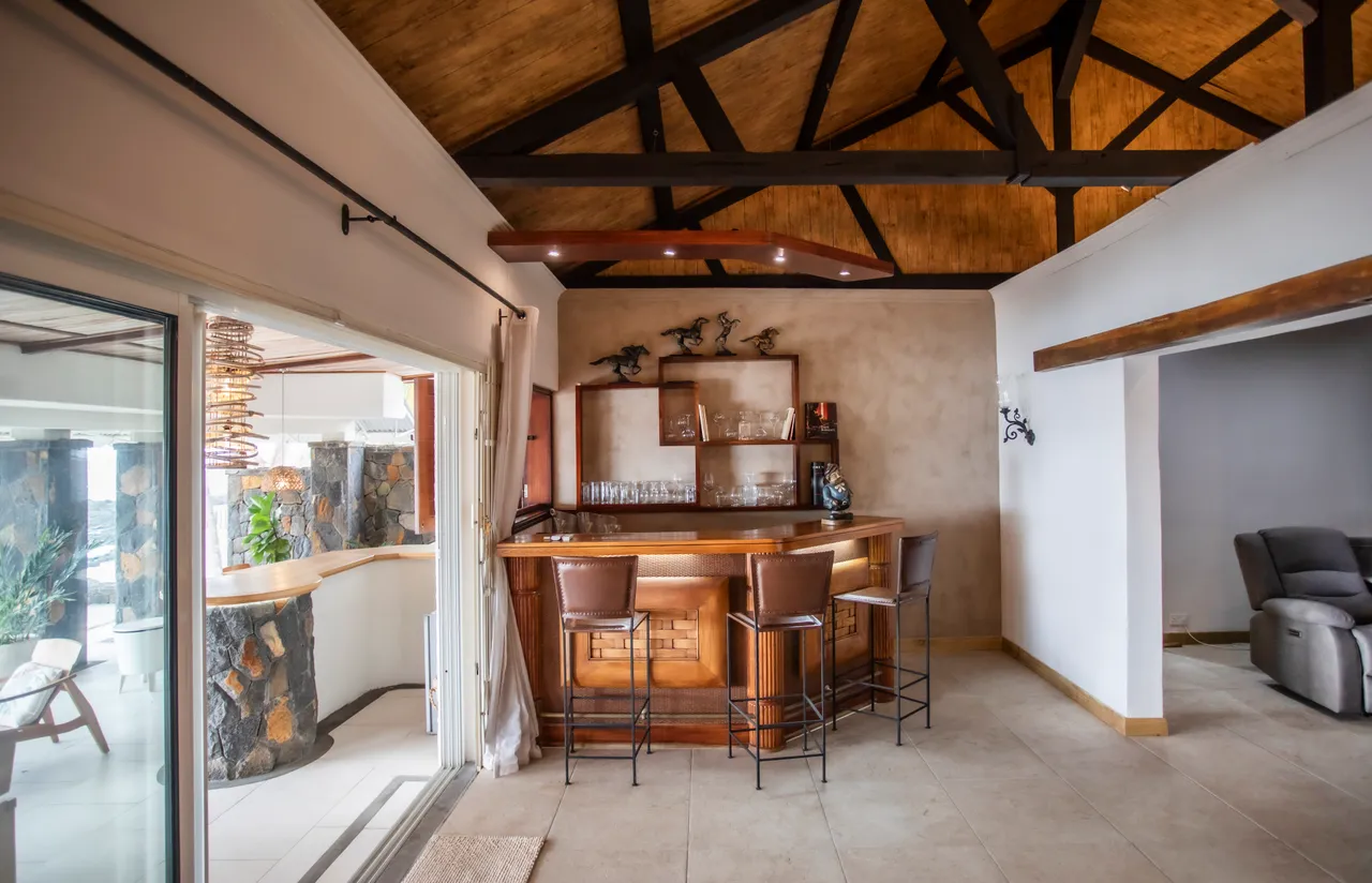 Espace bar en bois avec sièges en cuir, éclairage chaleureux au plafond. Accès à l'extérieur depuis la pièce.