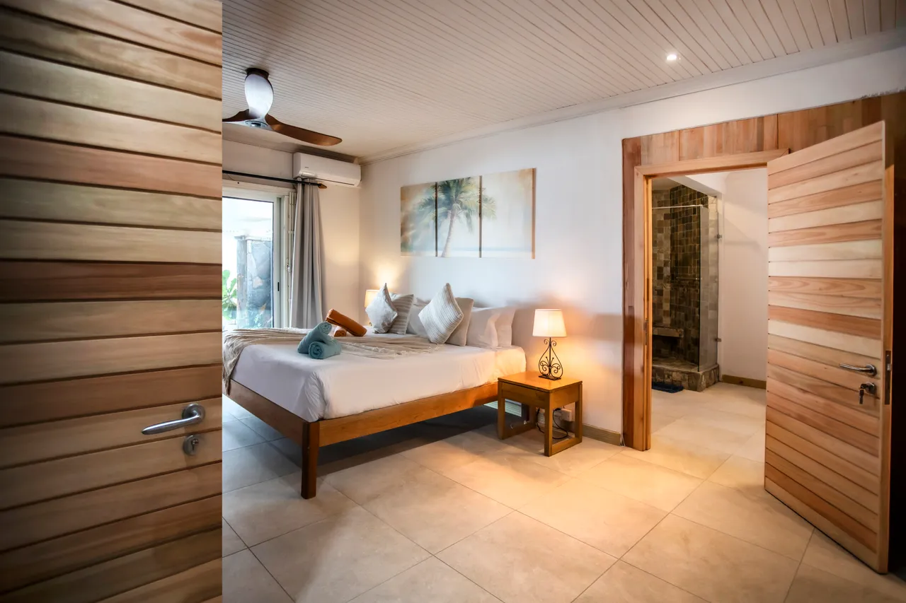 Chambre avec un lit double, tables de chevet et lampes. Salle de bain attenante avec douche en mosaïque.